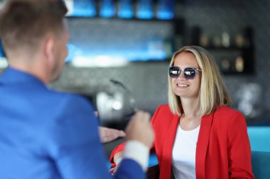 Kırmızı ceketli ve güneş gözlüklü neşeli kadın barda oturuyor..