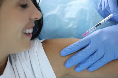 Lastik eldivenli doktor genç bir kadının omzuna ilaç enjekte ediyor.