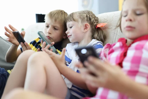 Children sit on couch and play smartphones.