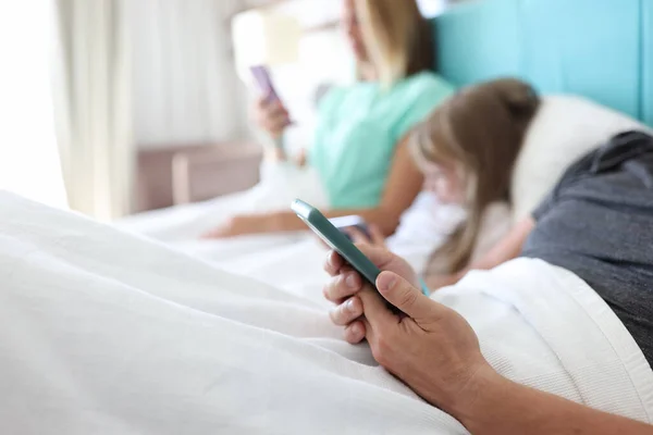 Сімейний чоловік жінка дитина лежить в ліжку, і кожен тримає смартфон в руках — стокове фото