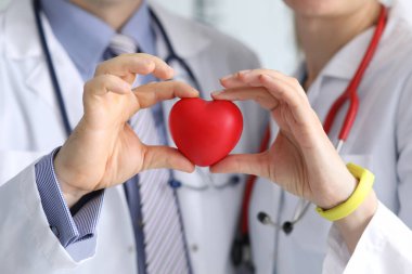 Doktor erkek ve kadın, ellerinde fonendoskopla kırmızı bir kalp tutuyorlar.