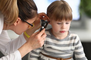 Kadın otorhinolaryngolog klinikte otoskopla küçük kızların kulaklarını inceliyor.