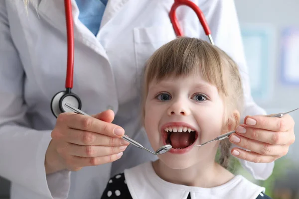 Tandarts met stethoscoop onderzoekt tanden van klein meisje in kliniek — Stockfoto