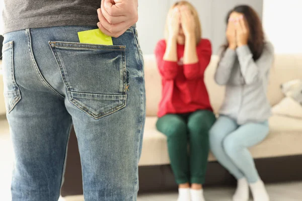 남성이 청바지 주머니에서 콘돔을 꺼내고, 두 여성이 반대로 앉아서 손으로 눈을 가리고 있습니다. — 스톡 사진