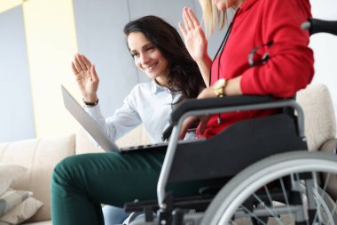 Tekerlekli sandalyedeki kadın arkadaşıyla internet üzerinden el sallıyor.