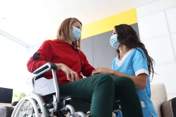 Лікар-фізіотерапевт тримає руку жінки в інвалідному візку в медичних масках — стокове фото