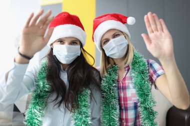 Kırmızı Noel şapkalı ve tıbbi maskeli kadınlar merhaba diyor.