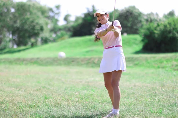 Schöne Frau in weißem Rock, Mütze und rosa T-Shirt spielt Golf auf grünem Rasen. — Stockfoto