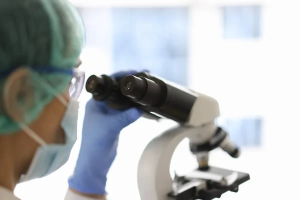 Laboratory assistant in protective suit look through microscope.