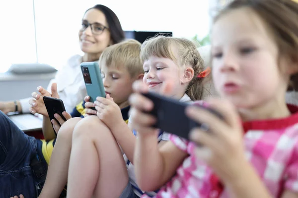 Трое детей сидят бок о бок на диване и играют на смартфонах. — стоковое фото