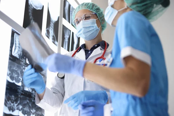 Deux médecins en costume, gants médicaux et masques de protection tiennent une photographie radiographique. — Photo