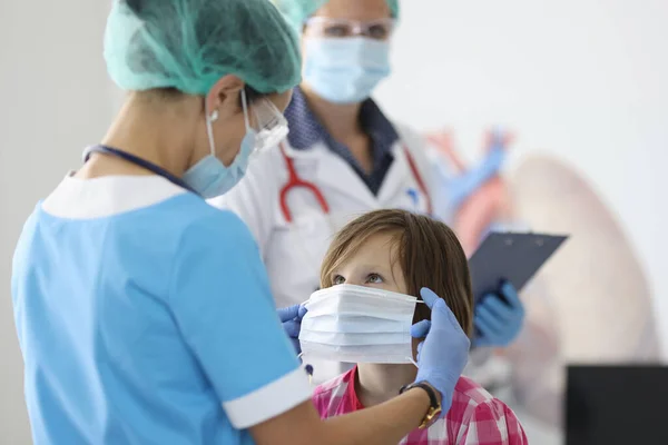 Lekarz w niebieskim garniturze i masce ochronnej umieścić maskę ochronną na twarzy dziewczyny. — Zdjęcie stockowe
