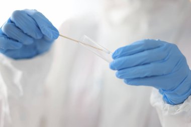 Doktorun elinde laboratuardaki tıbbi eldivenlerle test tüpü ve pamuk çubuğu var.