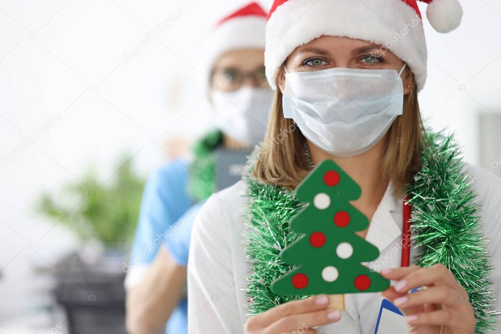 Young female doctors in santa claus hats and tinsel around their necks are holding christmas tree toy