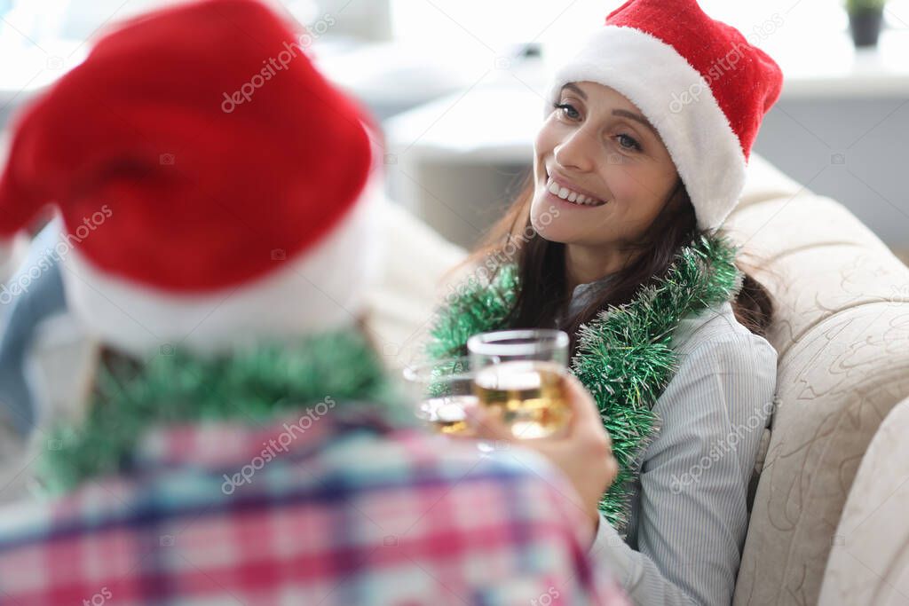 Woman in red santa claus hat drinks alcohol from glass with her friend