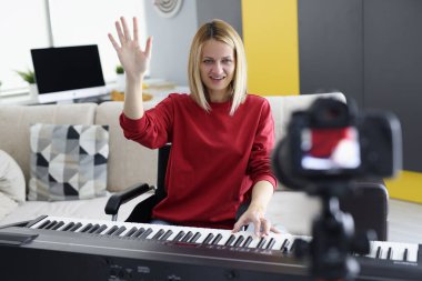 Tekerlekli sandalyedeki genç kadın piyano çalar ve elini sallar.