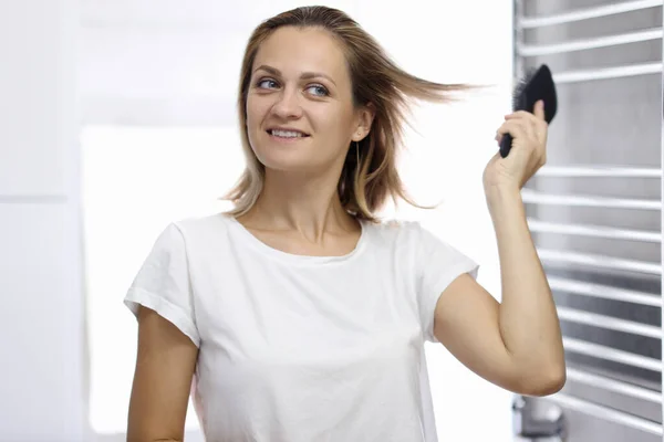 Jovem mulher bonita está olhando para o seu reflexo no banheiro e pentear o cabelo — Fotografia de Stock