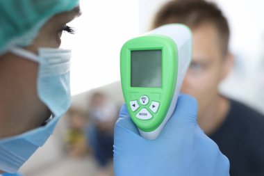Koruyucu tıbbi maskeli bir doktor hastanın sıcaklığını ölçer..
