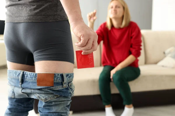 Hombre en pantalones cortos tirando de los pantalones vaqueros abajo se pone de pie con condón en la mano de cerca delante de la chica —  Fotos de Stock