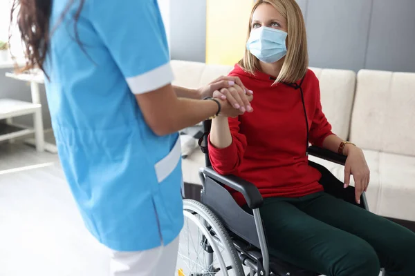 Médico en uniforme sostiene la mano de mujer joven enferma en retrato de silla de ruedas — Foto de Stock