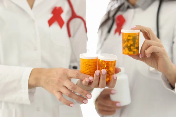 Doctors with red ribbon on uniforms are holding jars of medicines closeup