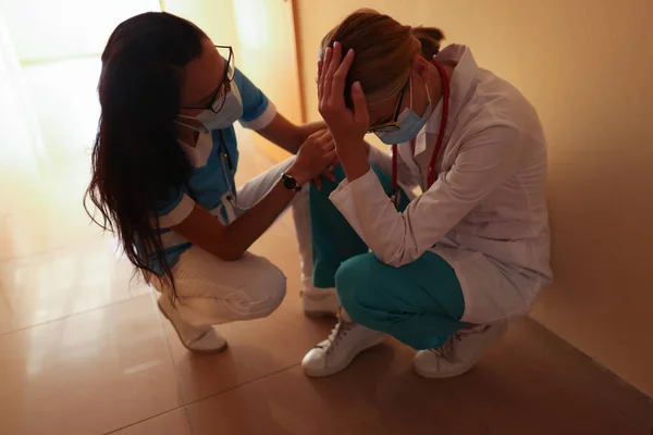 Sestra uklidňuje pláče lékař na sobě lékařské ochranné masky v jasné nemocniční chodbě. — Stock fotografie