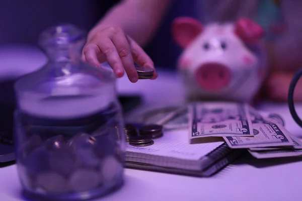 En la mesa hay alcancía, billetes de dólar, monedas en el banco y un montón de monedas en la mano. — Foto de Stock