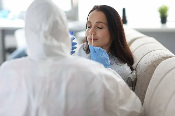 Medisch officier in beschermende pak neemt biologisch materiaal van vrouw met plank in haar mond. — Stockfoto