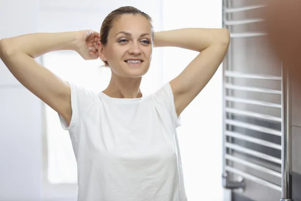 Frau im weißen T-Shirt steht vor Badezimmerspiegel und lächelt. — Stockfoto