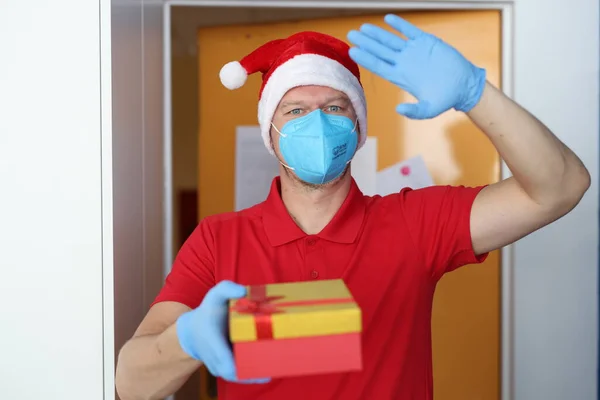 Man met blauwe masker en handschoenen houden doos met geschenk en zwaai hallo. — Stockfoto