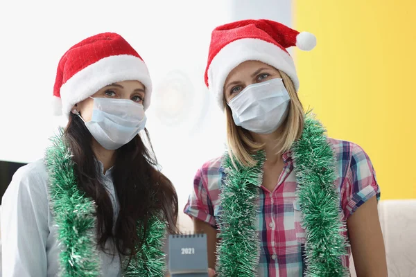 Dos mujeres en máscara protectora se sientan lado a lado y sostienen 2021 calendario. — Foto de Stock