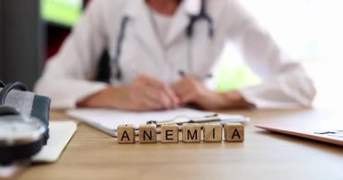 Tahta küpler hasta geçmişi yazan bir kadının yanında Anemia kelimesi oluşturur. Haber sağlık endişesi hissi getiriyor. Hastane atmosferi yaratıyor.