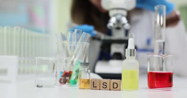 Tahta küpler, LSD 'nin psikoaktif madde araştırmalarına odaklandığını gösteriyor. Adli laboratuvar masasında renkli kimyasal sıvılar ve mikroskop var.