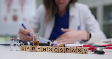Tıbbi uzman, laringospazm ve şırıngalı şişelerle blokların yanındaki masada yazıyor. Durum, ses tellerinin istemsiz kas spazmlarını içerir.