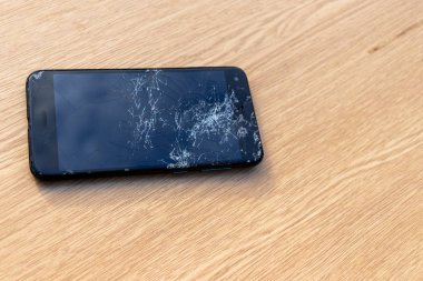 Hafif arka planda kırık ekran cep telefonu. Masanın üzerinde eski kırık siyah akıllı telefon. Cep telefonu onarım işlemini gösteren fotoğrafları kapatın. Akıllı telefon ve ahşap hummer. 