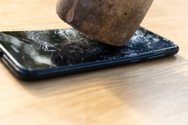 Hafif arka planda kırık ekran cep telefonu. Masanın üzerinde eski kırık siyah akıllı telefon. Cep telefonu onarım işlemini gösteren fotoğrafları kapatın. Akıllı telefon ve ahşap hummer. 
