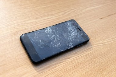 Hafif arka planda kırık ekran cep telefonu. Masanın üzerinde eski kırık siyah akıllı telefon. Cep telefonu onarım işlemini gösteren fotoğrafları kapatın. Akıllı telefon ve ahşap hummer. 