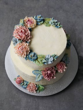 gri taş zemin üzerine buttercream çiçeklerle süslenmiş büyük düğün pastası