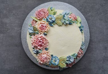 gri taş zemin üzerine buttercream çiçeklerle süslenmiş büyük düğün pastası