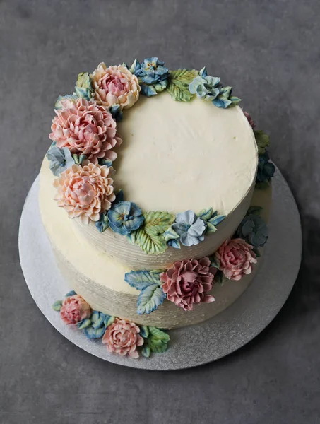 gri taş zemin üzerine buttercream çiçeklerle süslenmiş büyük düğün pastası