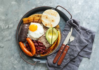 Colombian food. Bandeja paisa, typical dish at the Antioquia region of Colombia - fried pork belly , black pudding, sausage, arepa, beans, fried plantain, avocado egg, and rice. clipart