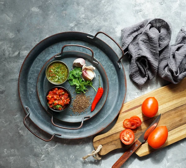 colombian food, aji picante, hogao salsa, on the metal tray and ingredients for souce, on the grey concrete backdrop, copy space for design text