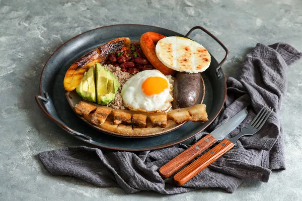 Colombian food. Bandeja paisa, typical dish at the Antioquia region of Colombia - fried pork belly , black pudding, sausage, arepa, beans, fried plantain, avocado egg, and rice.