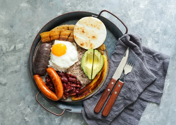 Colombian food. Bandeja paisa, typical dish at the Antioquia region of Colombia - fried pork belly , black pudding, sausage, arepa, beans, fried plantain, avocado egg, and rice.