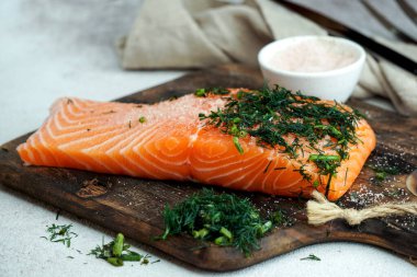 Kesme tahtasında tuz ve dereotlu taze somon balığı var.