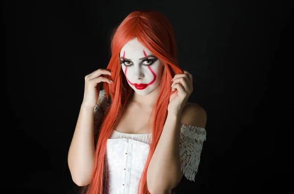 a girl in a clown costume with scary makeup on a black background