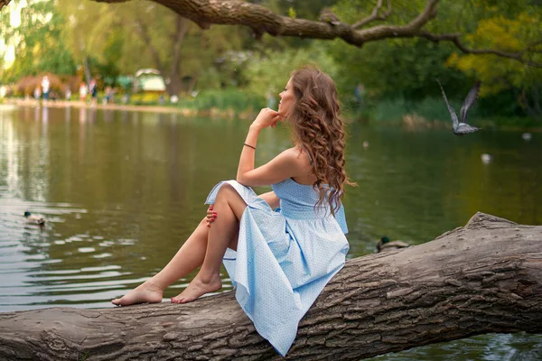 Girl sits on tree back and looks at lake.
