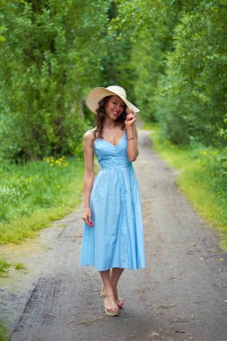 Hasır şapkalı ve mavi elbiseli güzel bir kız. Park yolunda. Kıvırcık esmer, yüzünde bir gülümsemeyle..