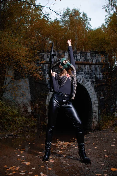 Una mujer en traje negro y máscara de gas con una ametralladora en las manos. — Foto de Stock