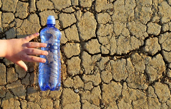 孩子的手到达一瓶水躺在干燥开裂的土壤上 全球变暖后果的概念 — 图库照片